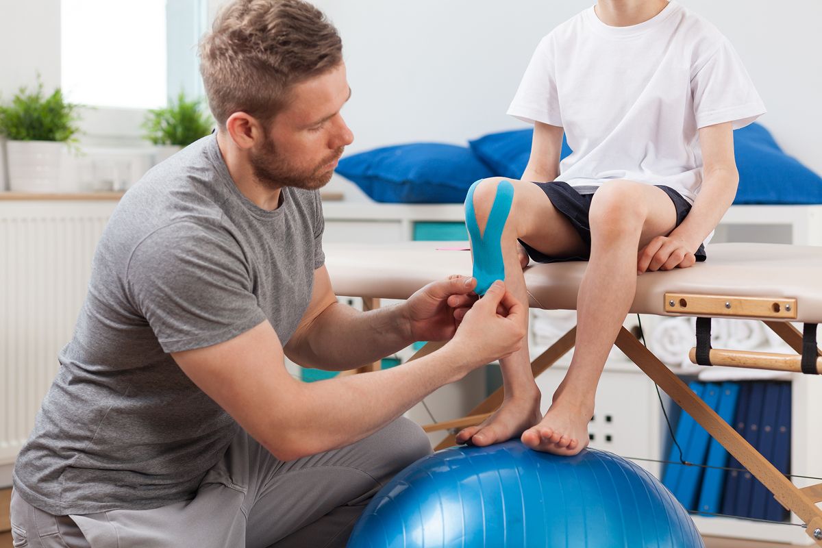Physiotherapeut verbindet ein Kind mit Kinesiologie-Tape